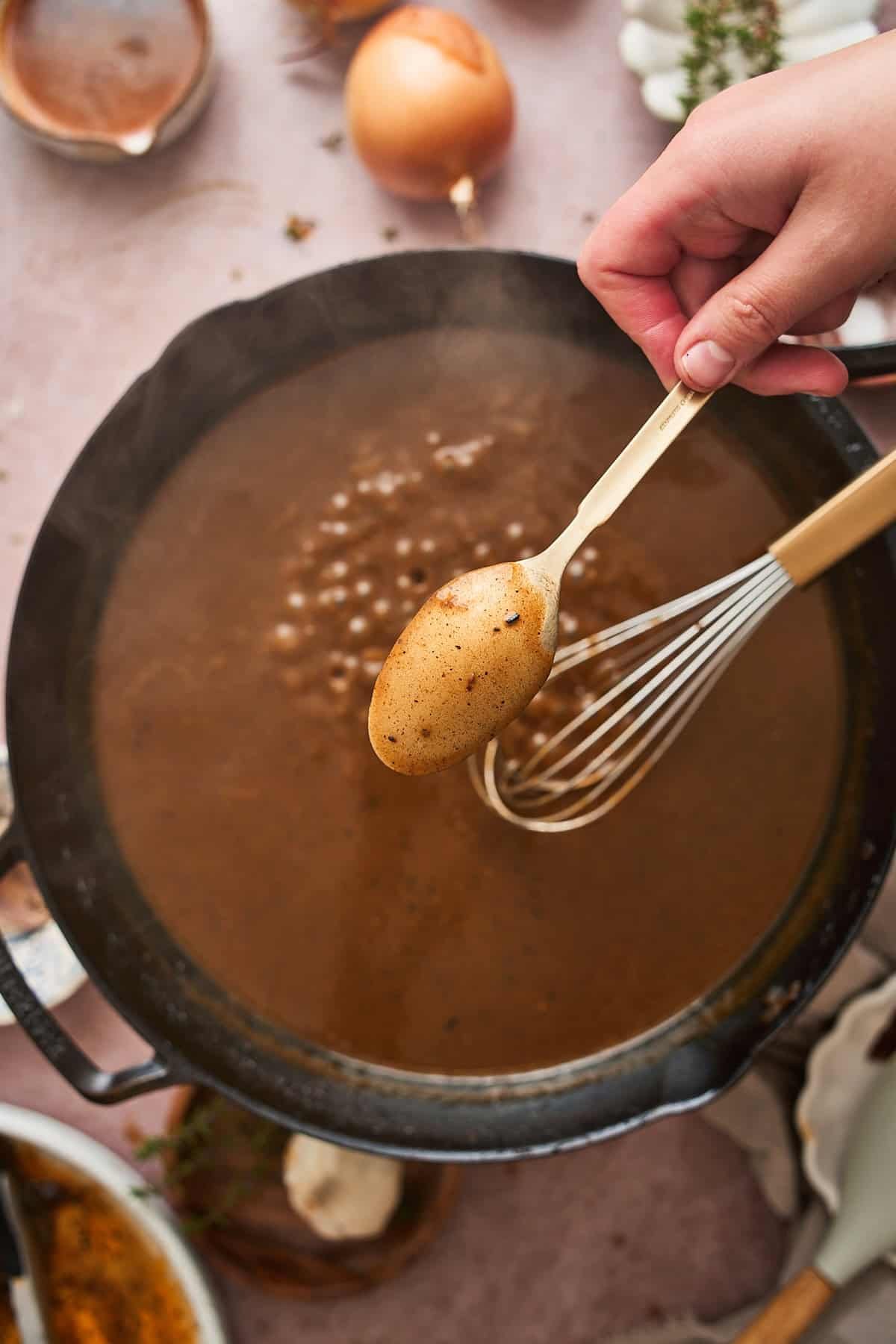 Gravy in a skillet with a whisk in the pan, and holding a spoon up to the camera to show the thickness of the gravy.