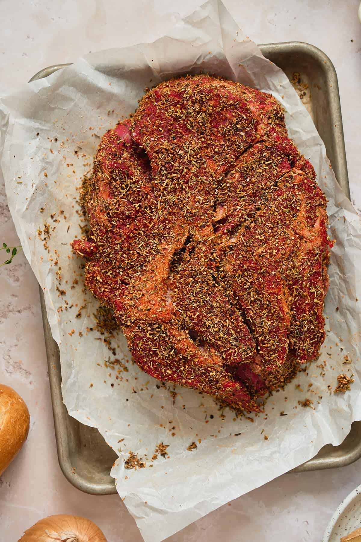 Raw chuck roast seasoned on a baking sheet with parchment.