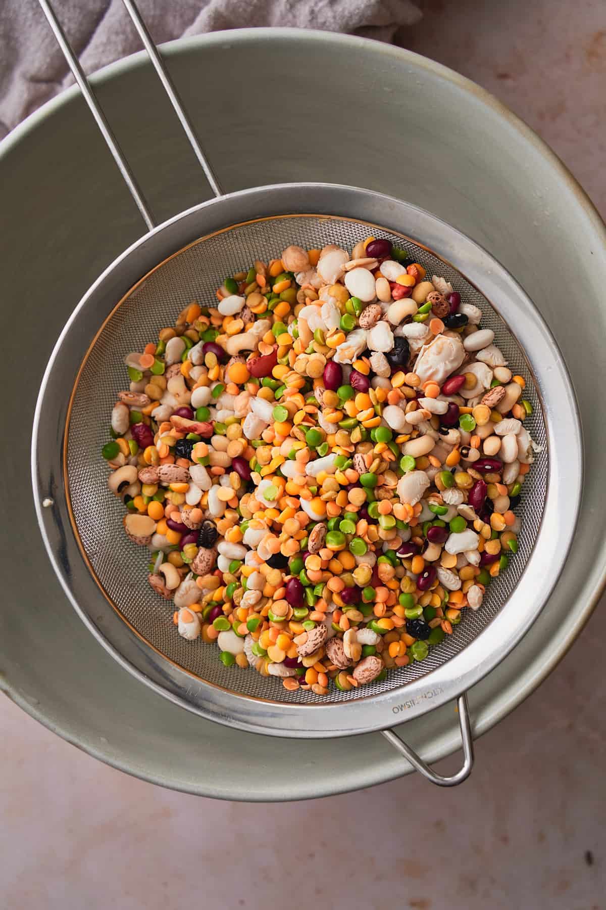 Beans being drained through a metal sieve above a large bowl of water.