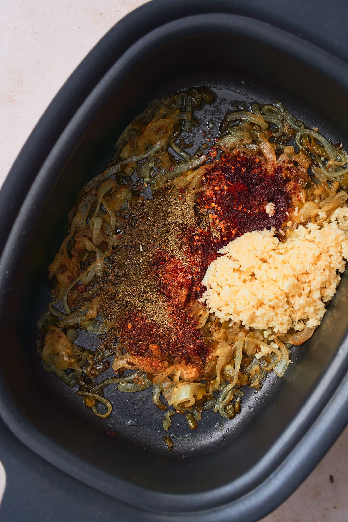 Onions cooked in butter in the bottom of a slow cooker, with lots of fresh garlic, smoked paprika, red pepper flakes, and dried thyme added to the onions.