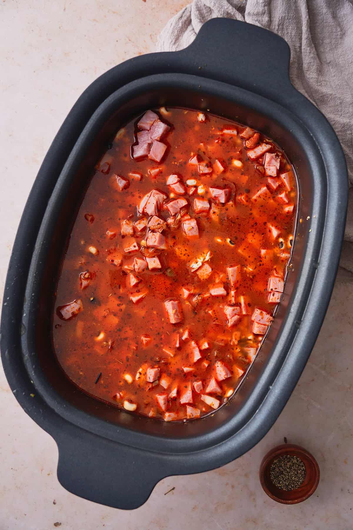 Slow cooker with a red, flavorful broth with ham and beans added to it.