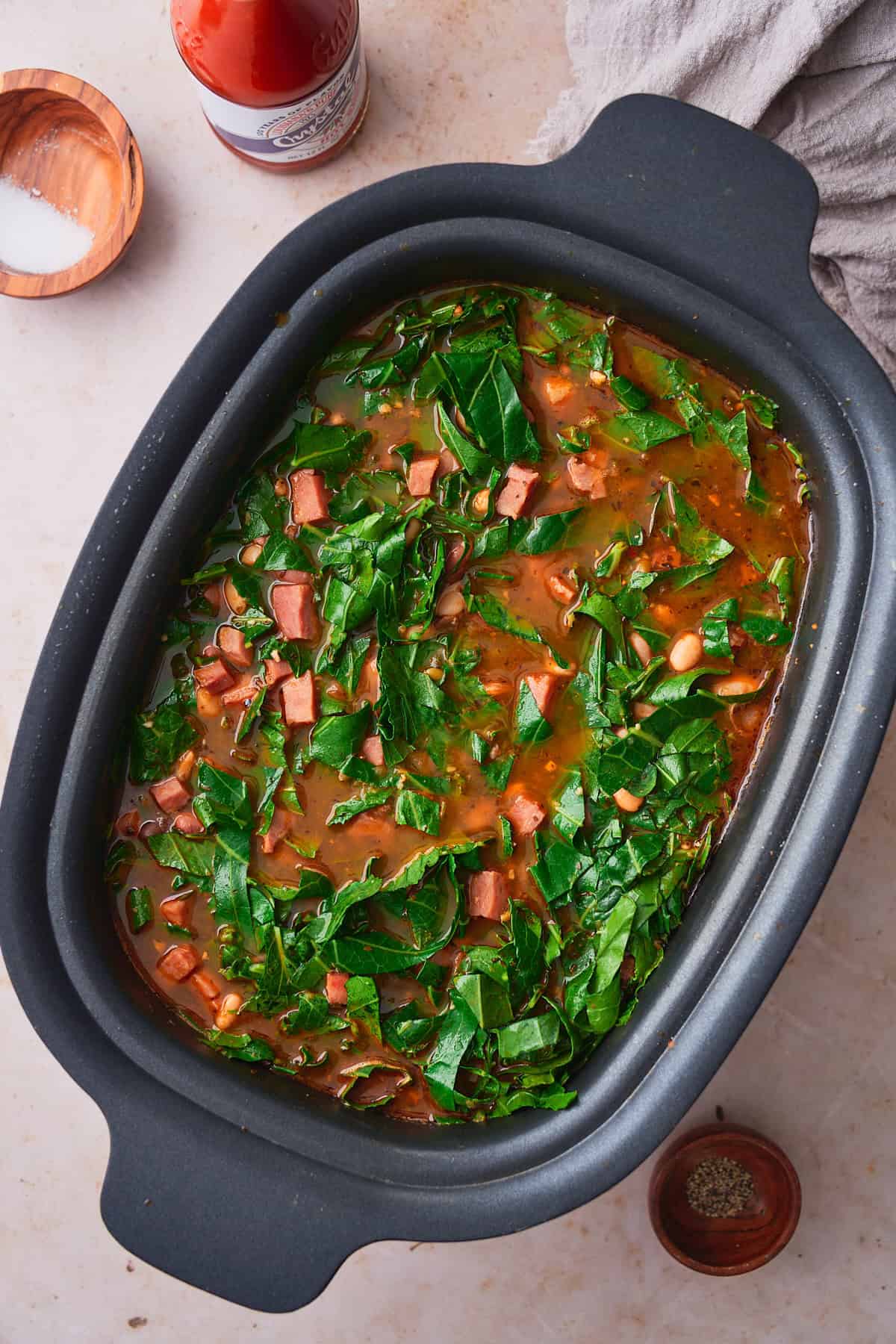 Collard greens added to a slow cooker with beans and ham.