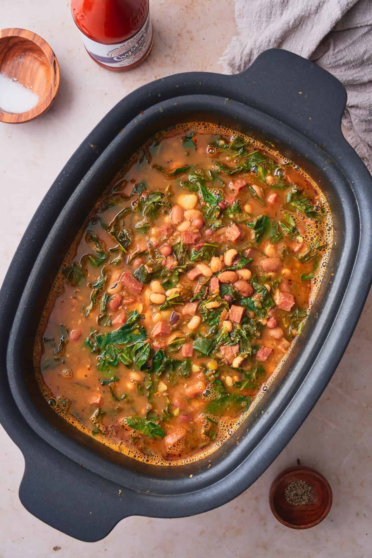 Cooked collard greens, beans and ham soup in a slow cooker.