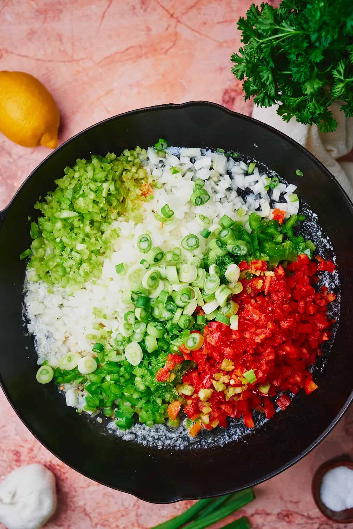 Bell peppers, onions, and celery in a cast iron skillet getting ready to be cooked down.