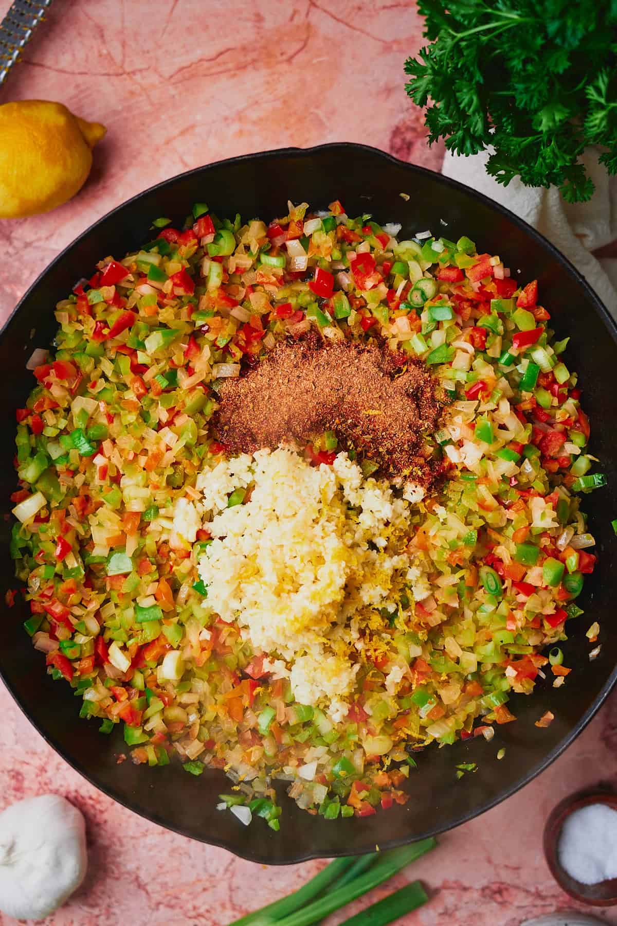 Cooked bell peppers onions and celery in a cast iron skillet with garlic, cajun seasoning, and lemon zest added.