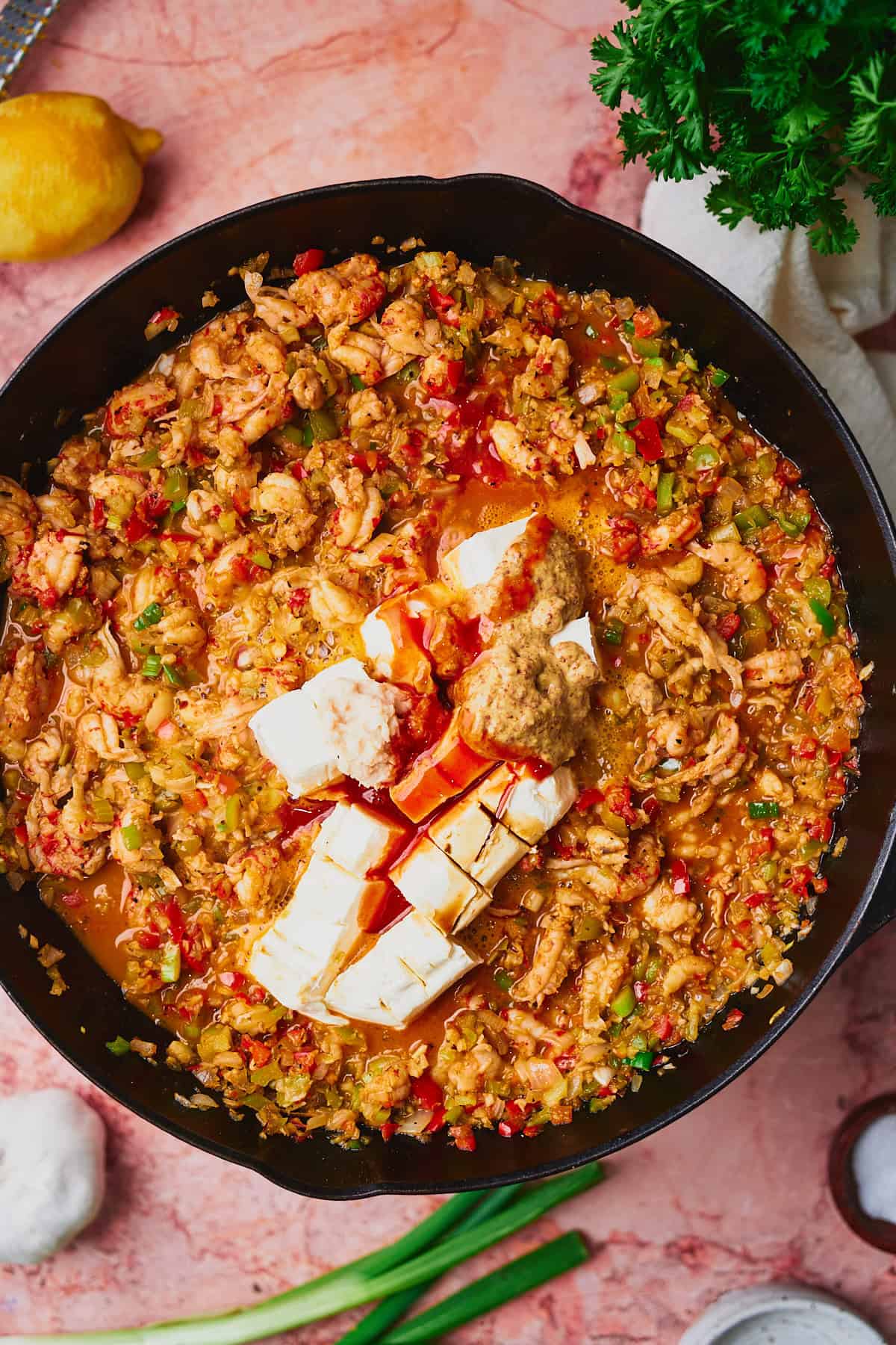 Cooked crawfish, peppers, onions, and aromatics in a cast iron skillet with cream cheese, mustard, and hot sauce added.