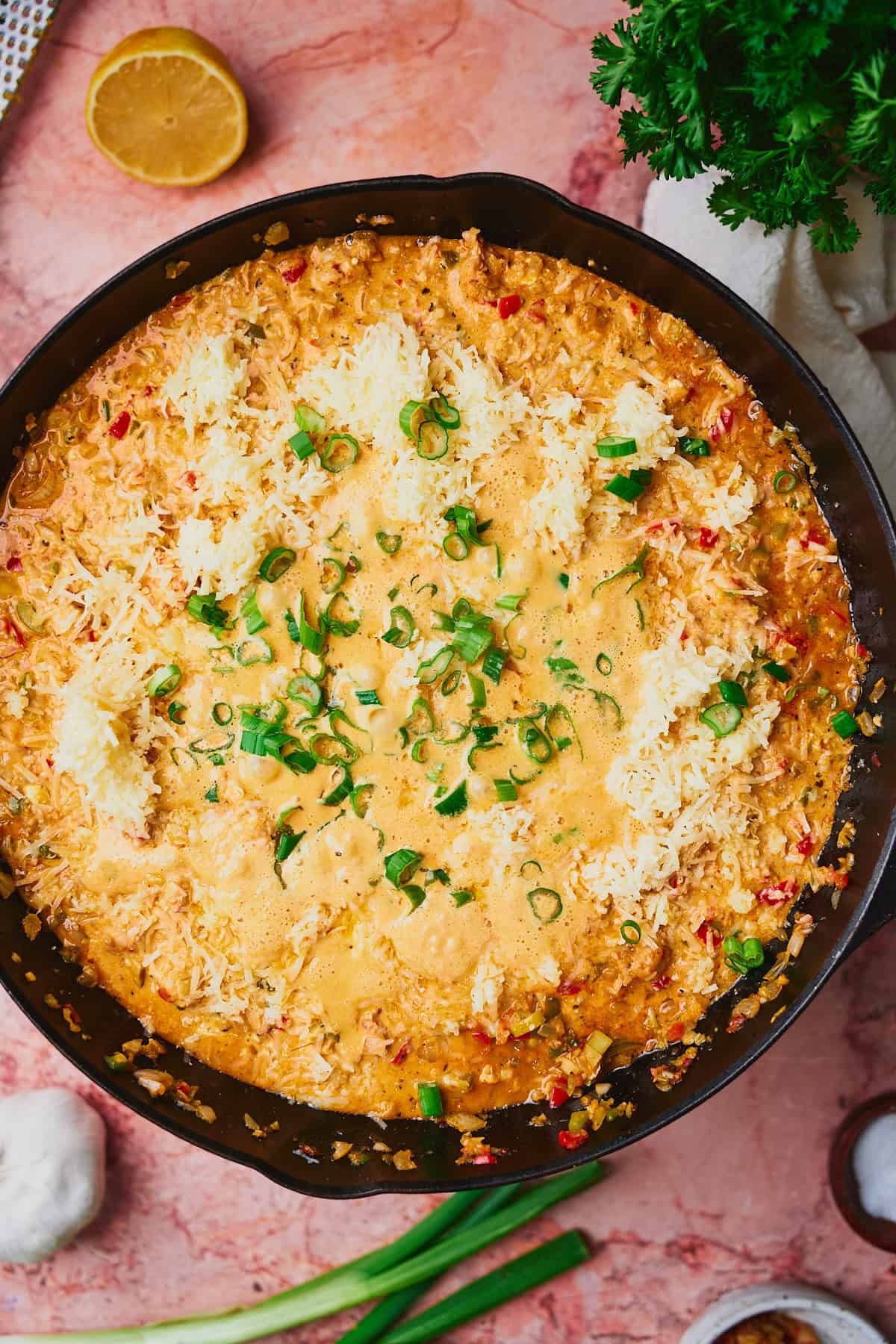 Cheese melting and added to a cast iron skillet with a creamy dip inside and topped with green onions.