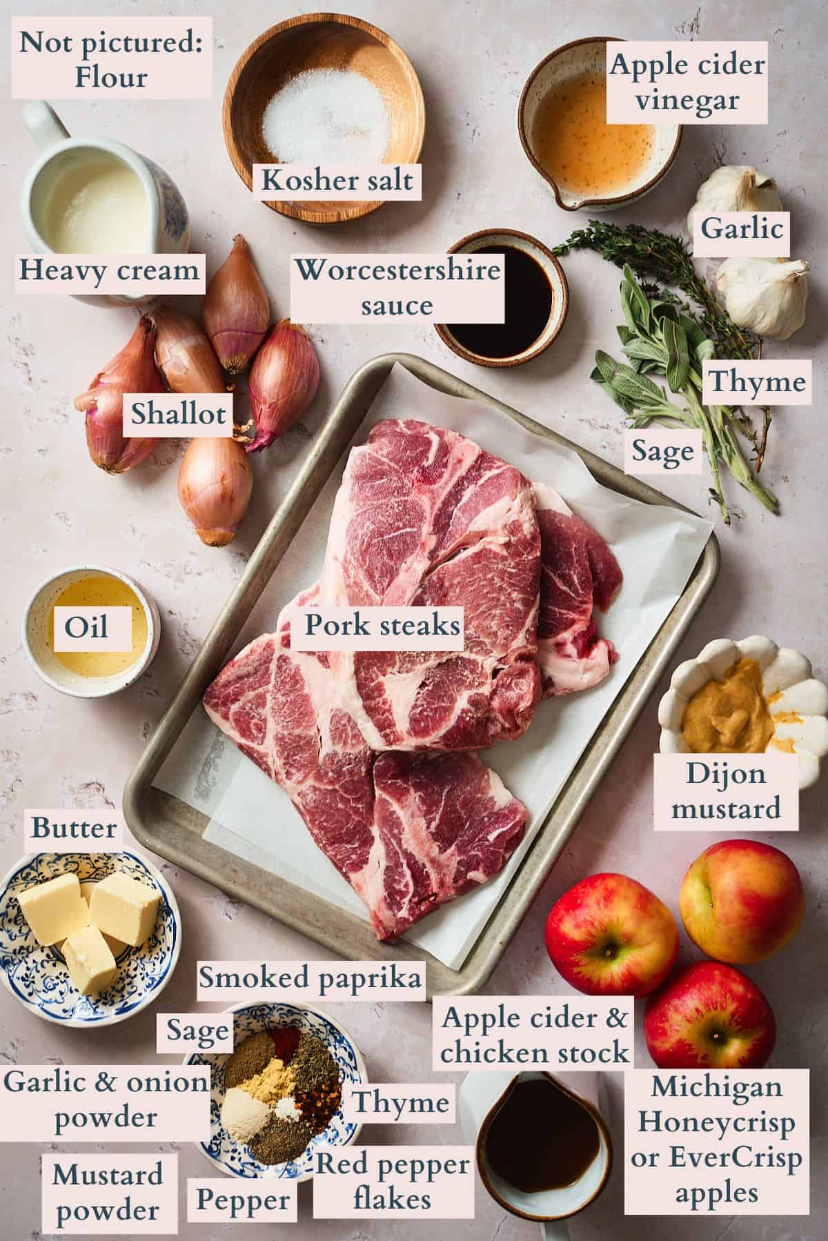 Ingredients to make creamy braised pork steaks and apples laid out on a table labeled to denote each ingredient.