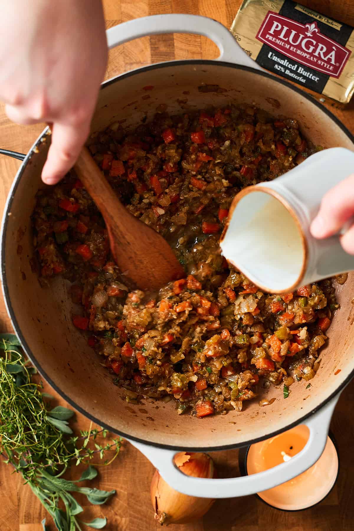 Hand pouring in white wine into a pot with veggies and flour mixture.