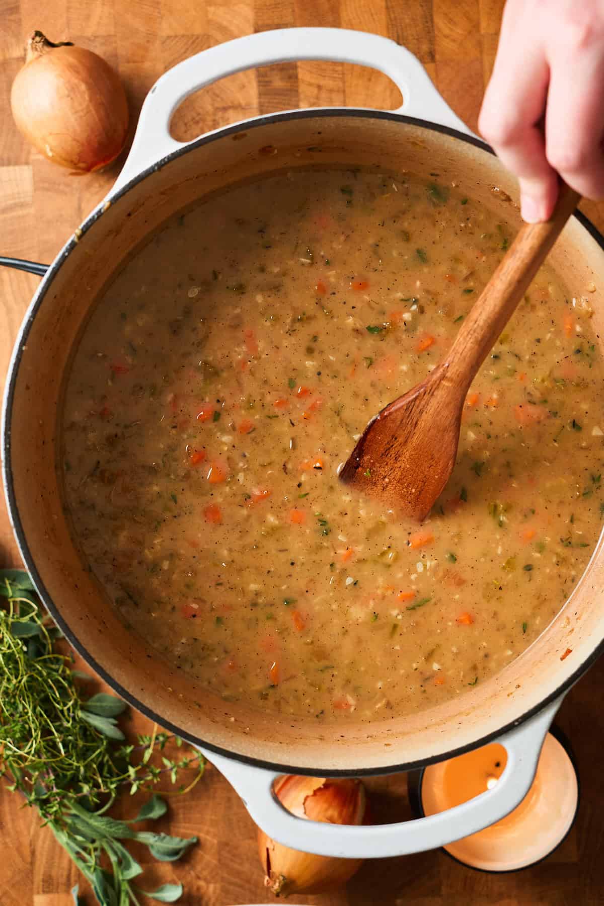 Hand stirring a wooden spoon in a pot of creamy stew.