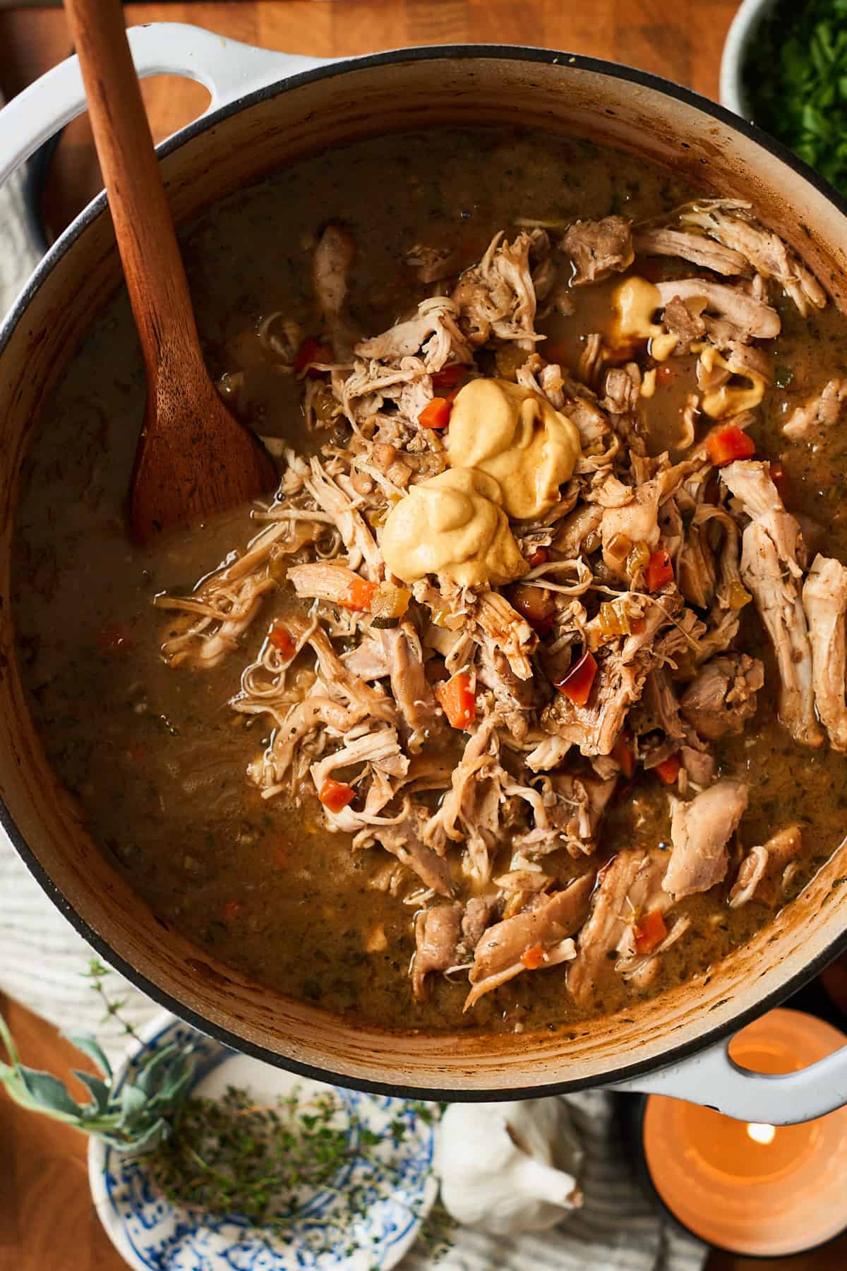 Adding shredded chicken thighs to a Dutch oven with a stew inside.