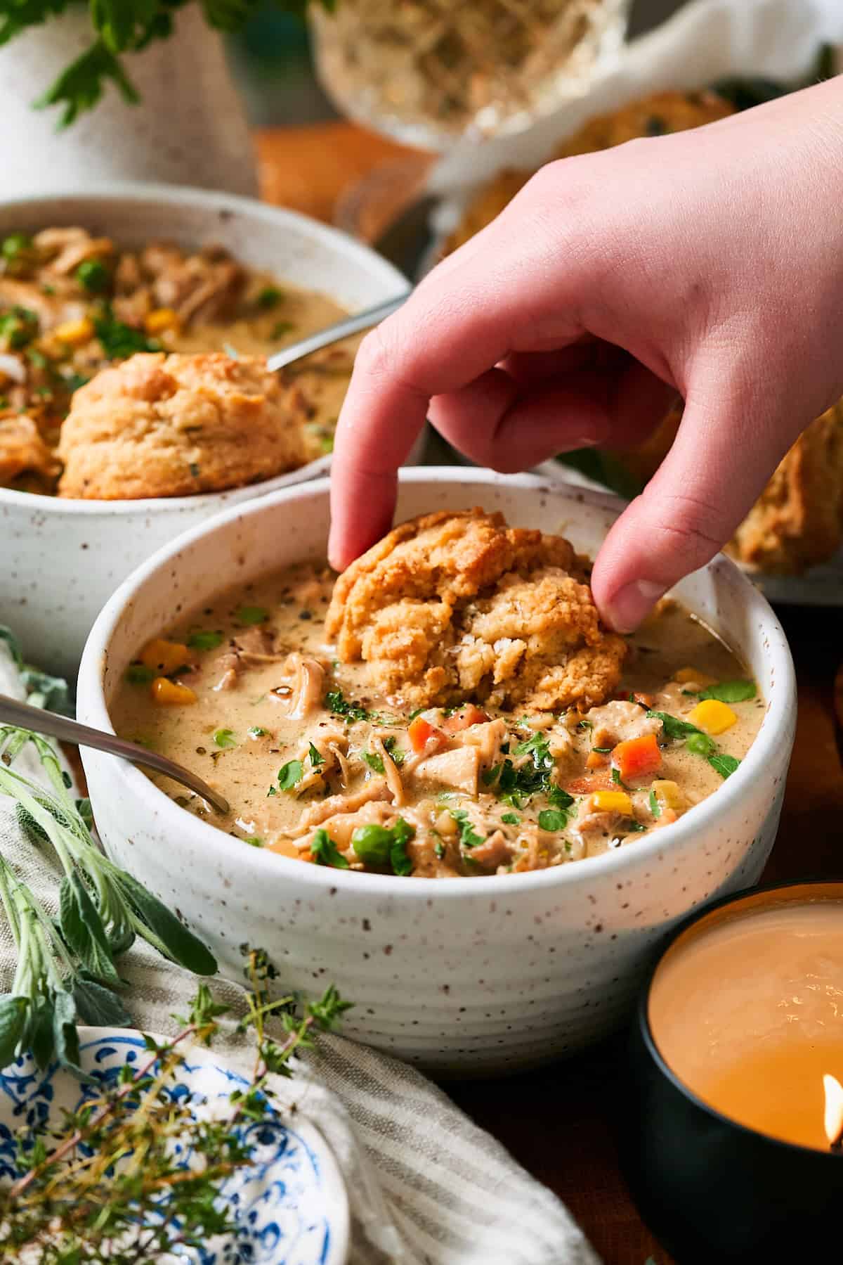 Hand dunking a drop biscuit into a bowl of creamy chicken pot pie soup.