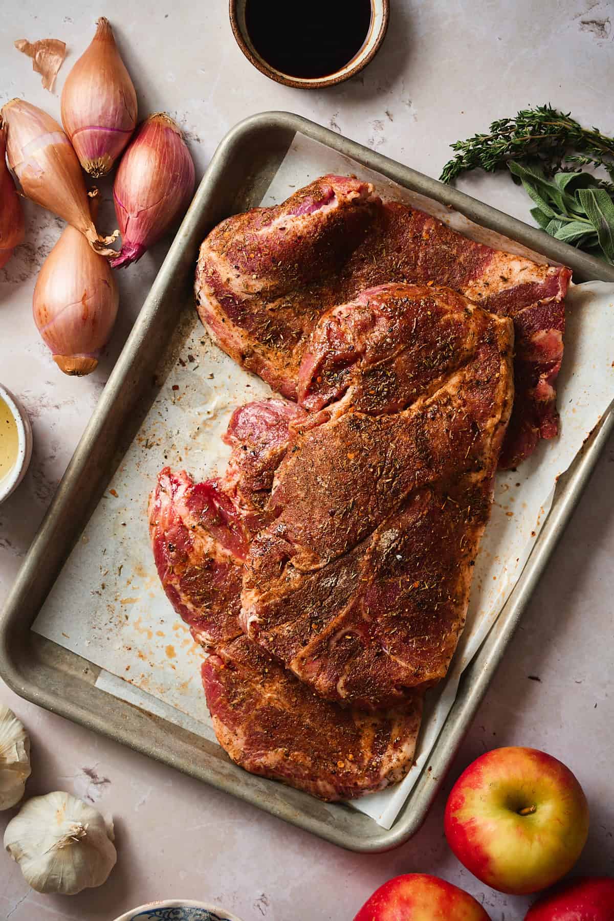 Seasoned raw pork steaks surrounded by apples shallots and other ingredients.