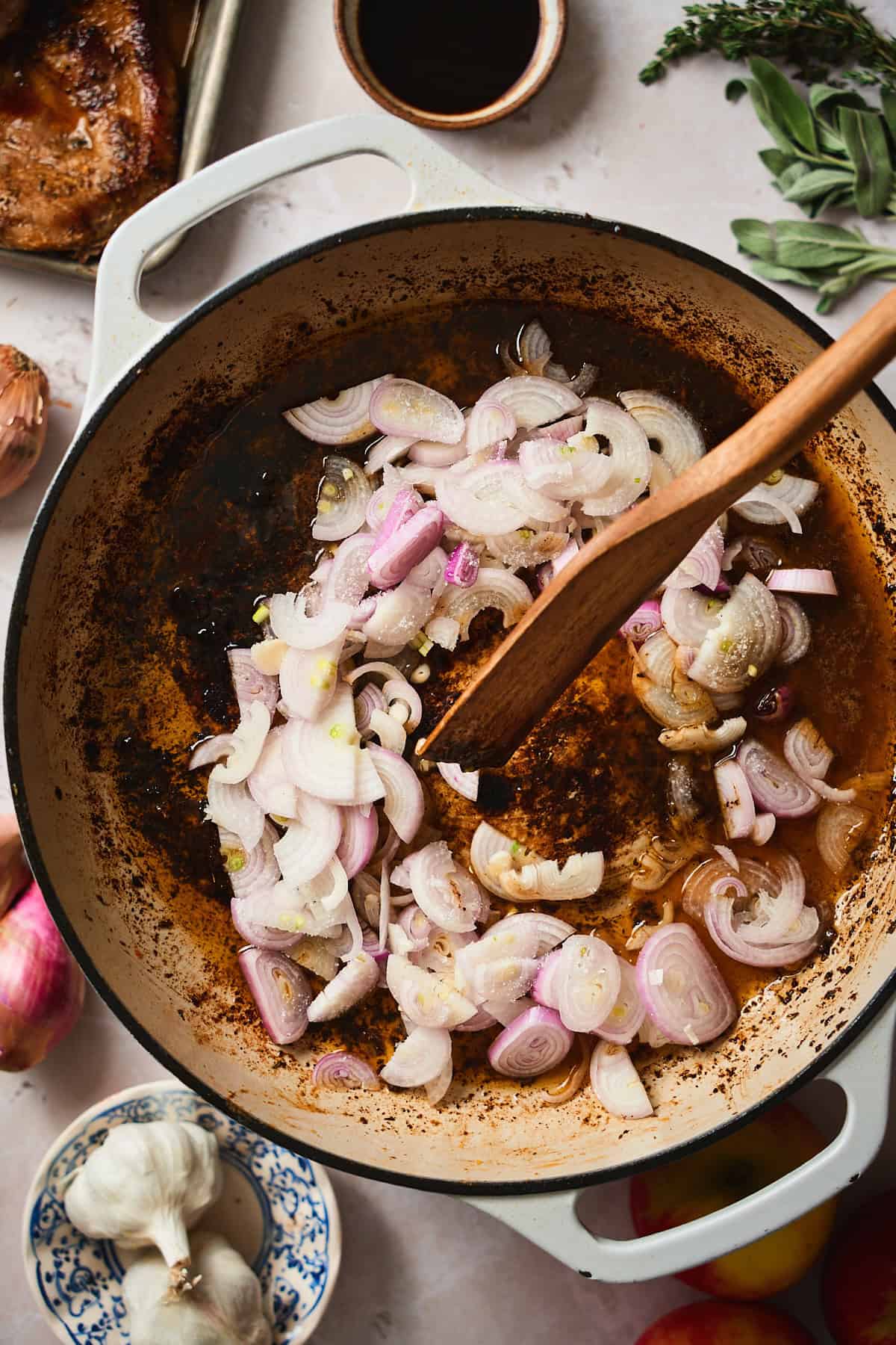 Shallots in an enameled skillet with a wooden spoon stirring them.