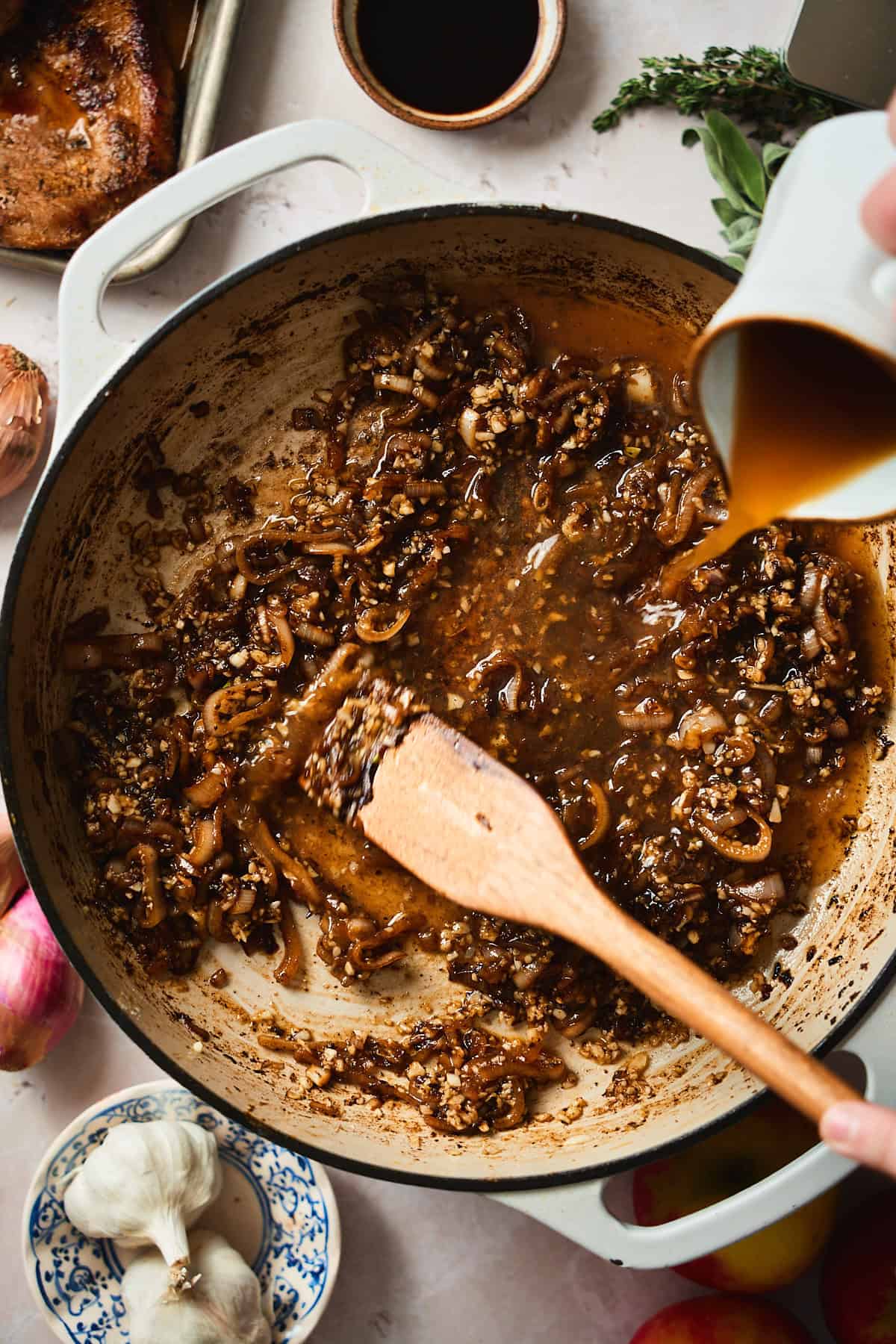 Stirring in apple cider to a skillet full of cooked shallots, pan drippings, and garlic.