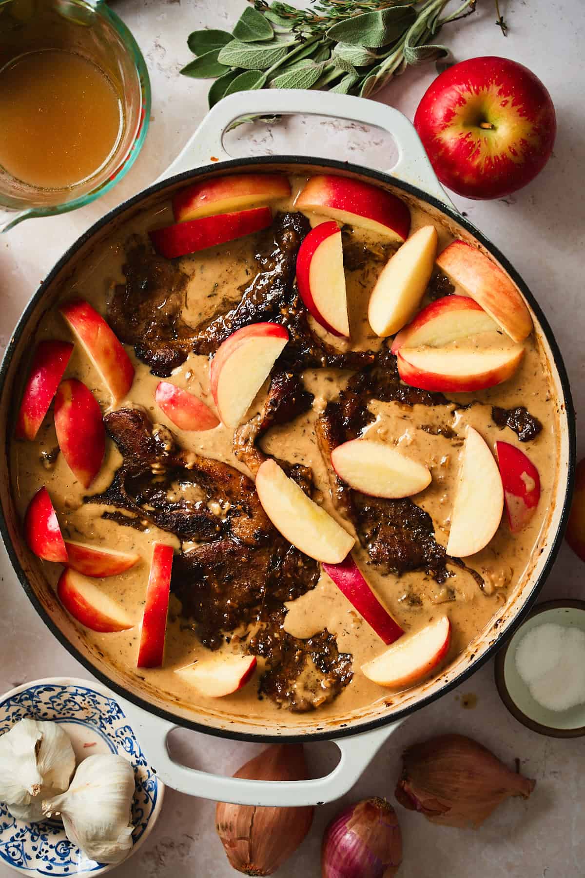 Pork steaks and apples added to a skillet with creamy gravy.