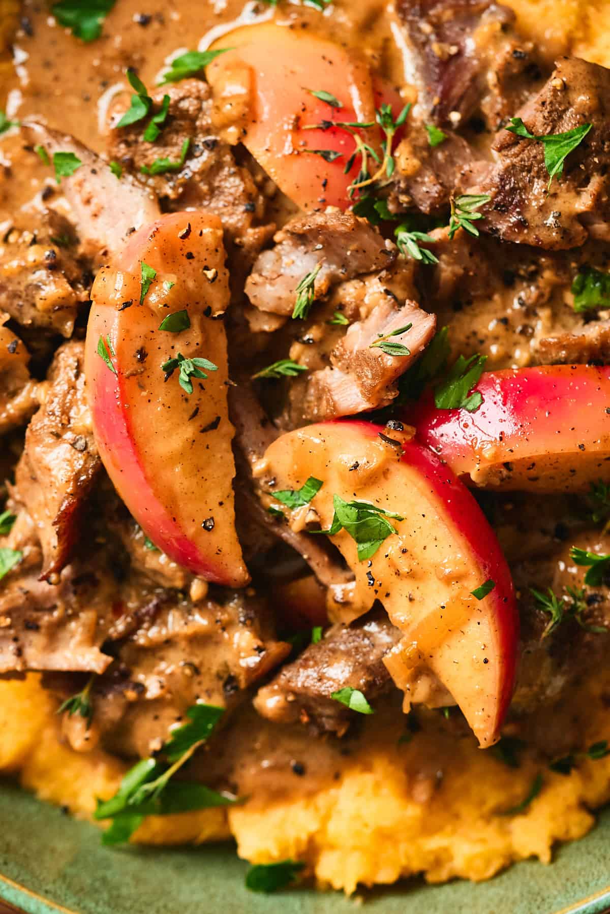 Close up shot of tender pork pieces with apples and rich gravy on top of mashed rutabaga with thyme, black pepper, and parsley.