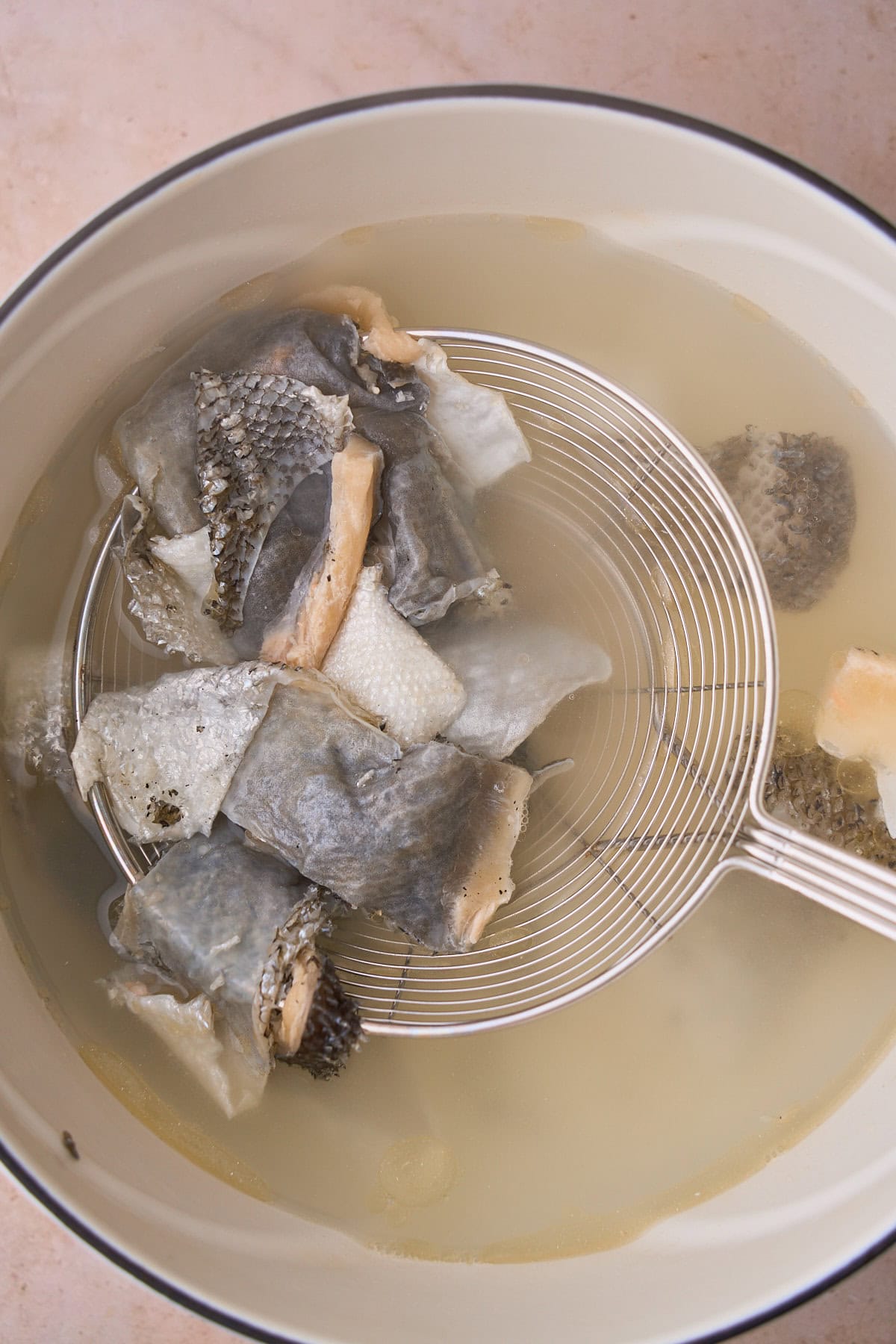 Salmon skins in a stockpot with a metal skimmer removing the skins from the stockpot.