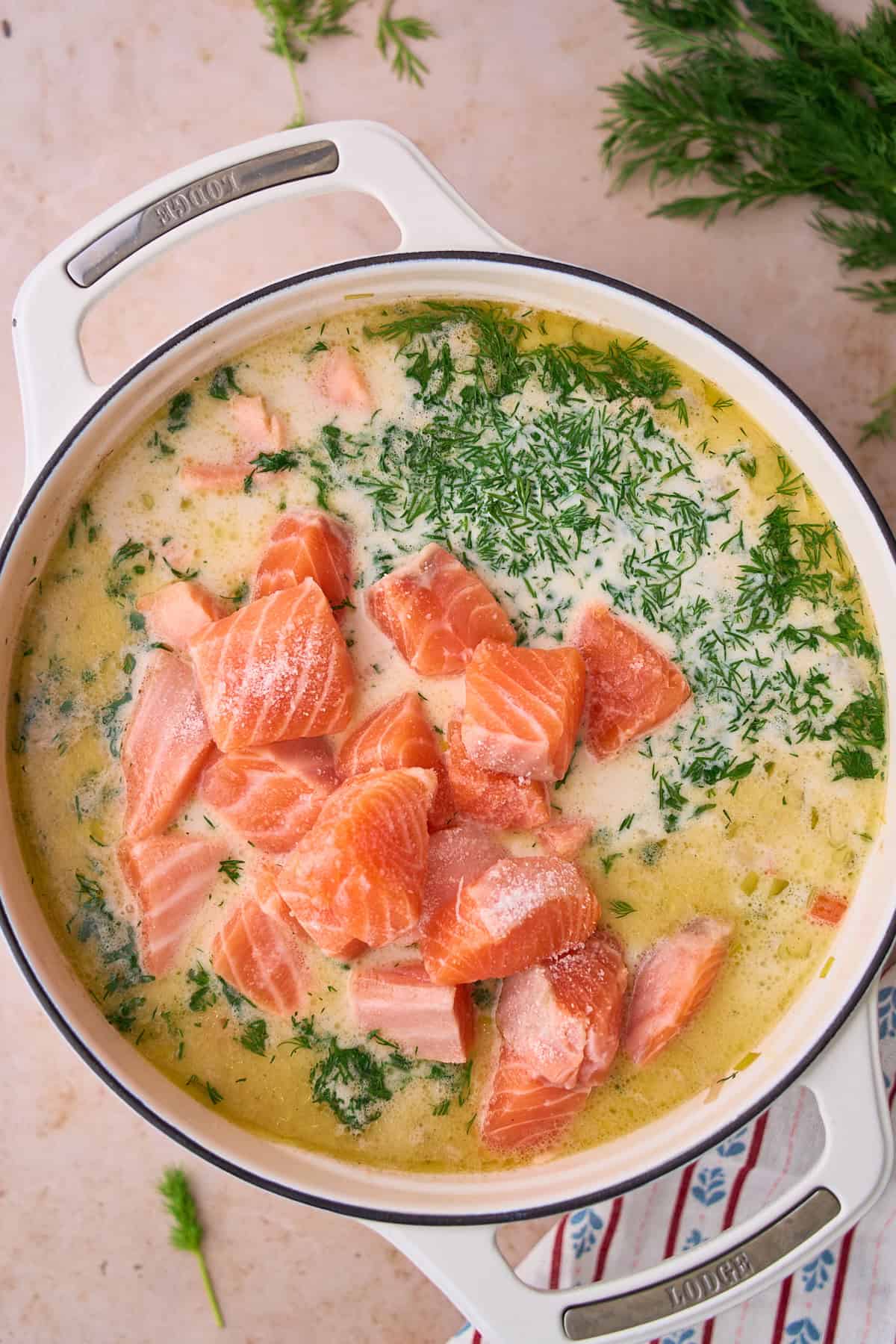 Raw salmon added to a soup pot with heavy cream, and dill added.