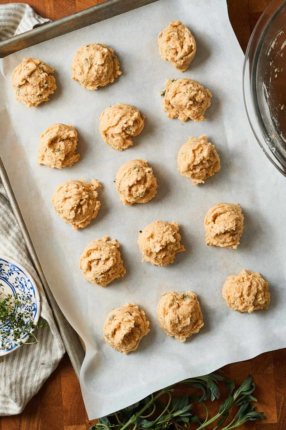 Biscuits scooped perfectly onto a tray with parchment paper, surrounded by herbs and candles.