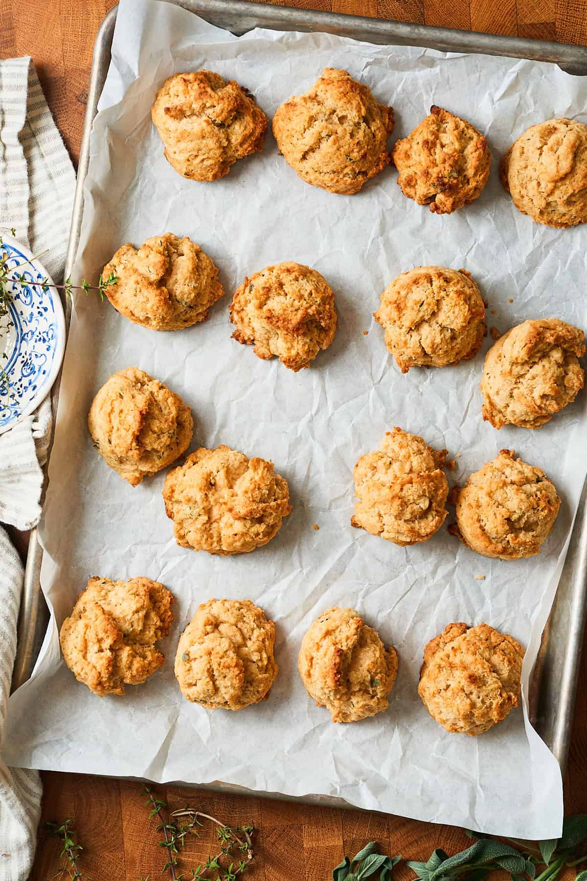 Baked herb brown butter drop biscuits on a baking sheet with herbs and a candle nearby.