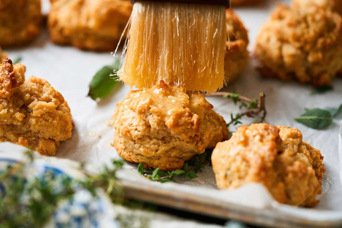 Brushing the top of an herbed drop biscuit with melted butter surrounded by fresh thyme and sage.