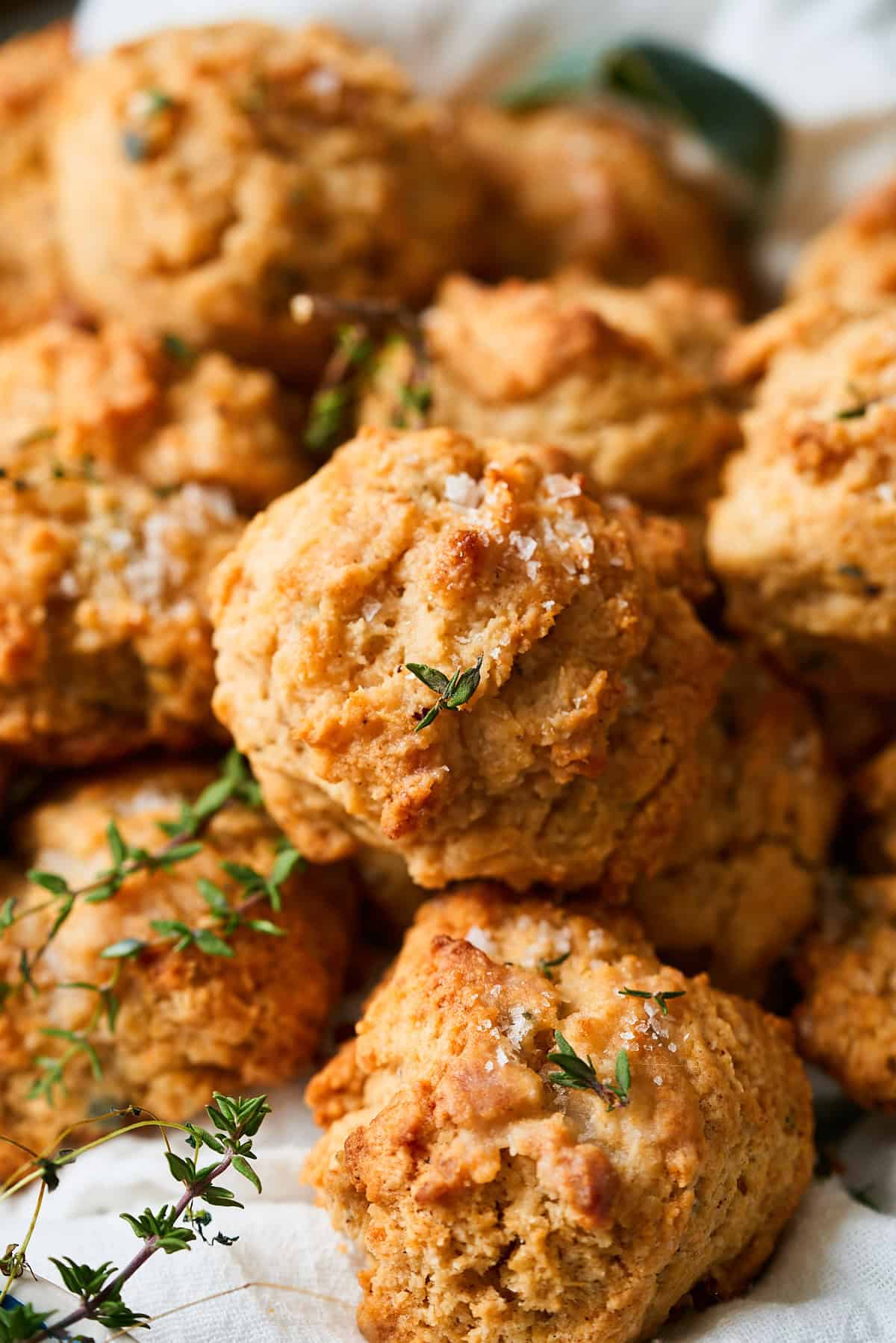 Close up macro shot of a pile of drop biscuits topped with flaky salt, fresh thyme, and sage.