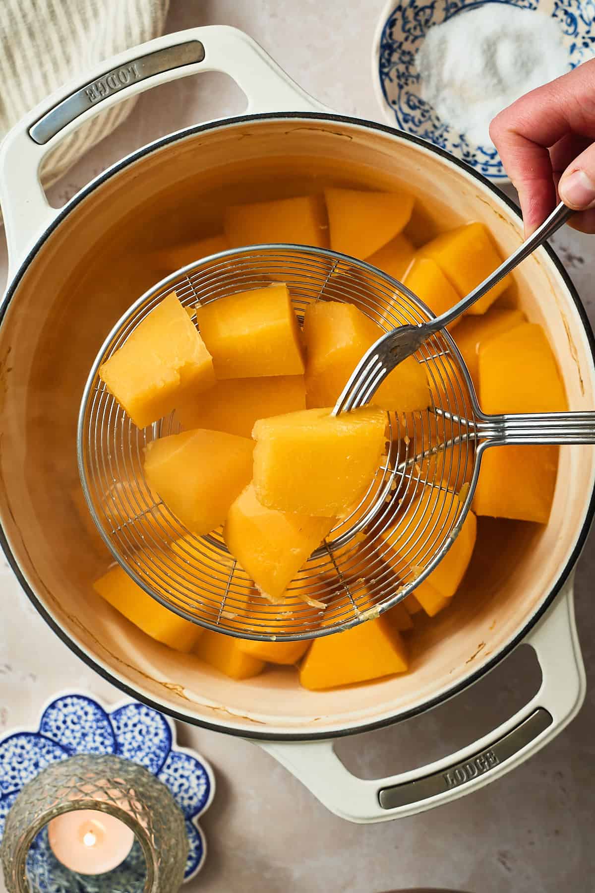 Photo of cooked rutabaga being held up with a metal sieve and a fork piercing it.