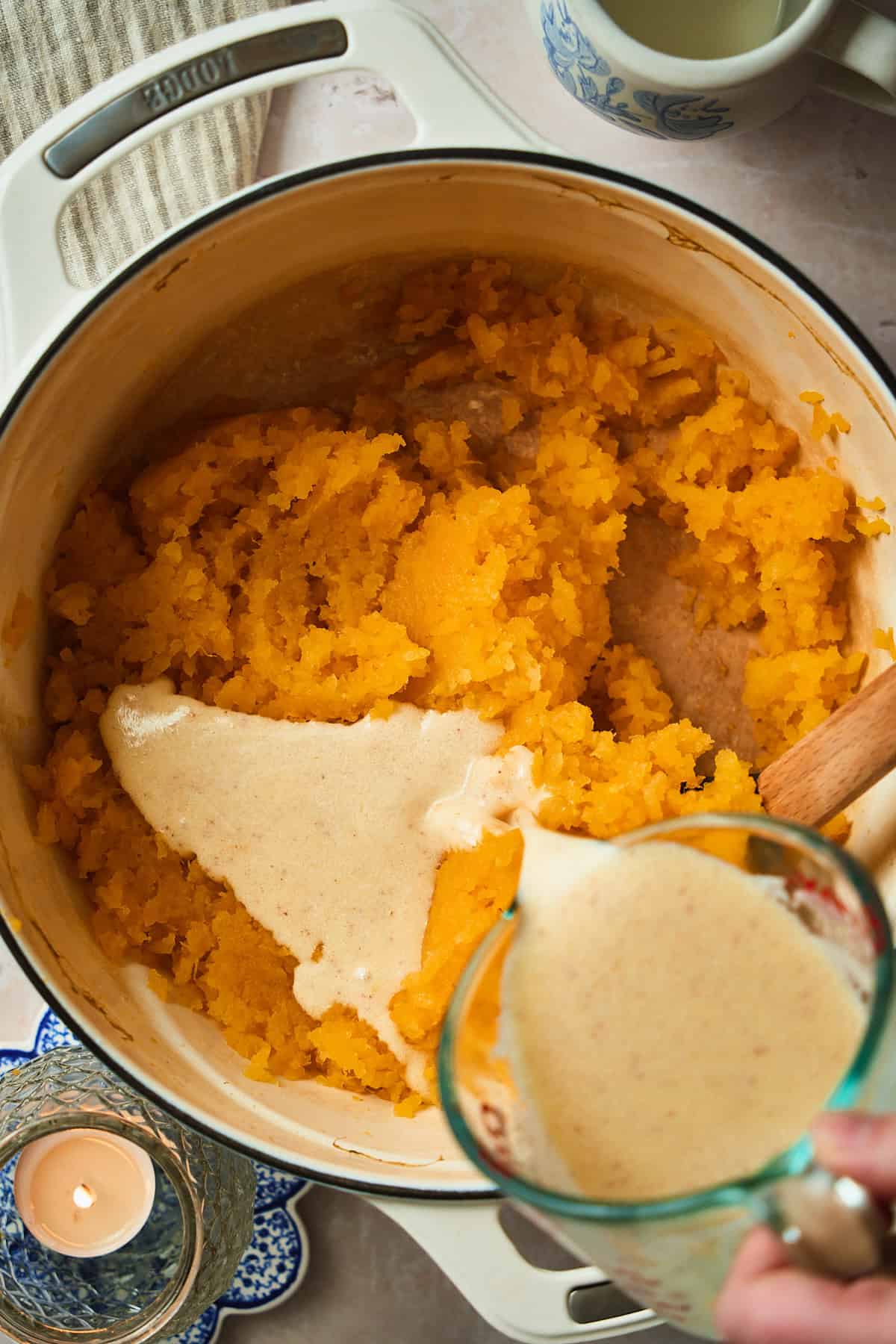 Pouring cream and butter into a mashed rutabaga mixture in a Dutch oven.