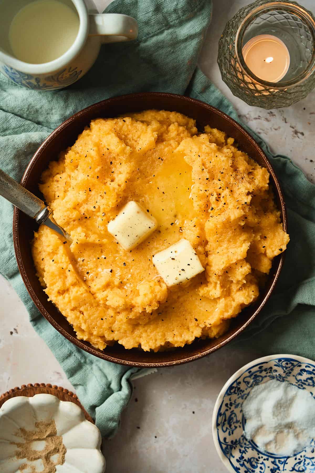Overhead view of a bowl of mashed rutabaga with butter melting into it, with flecks of black pepper surrounding and a blue napkin underneath.