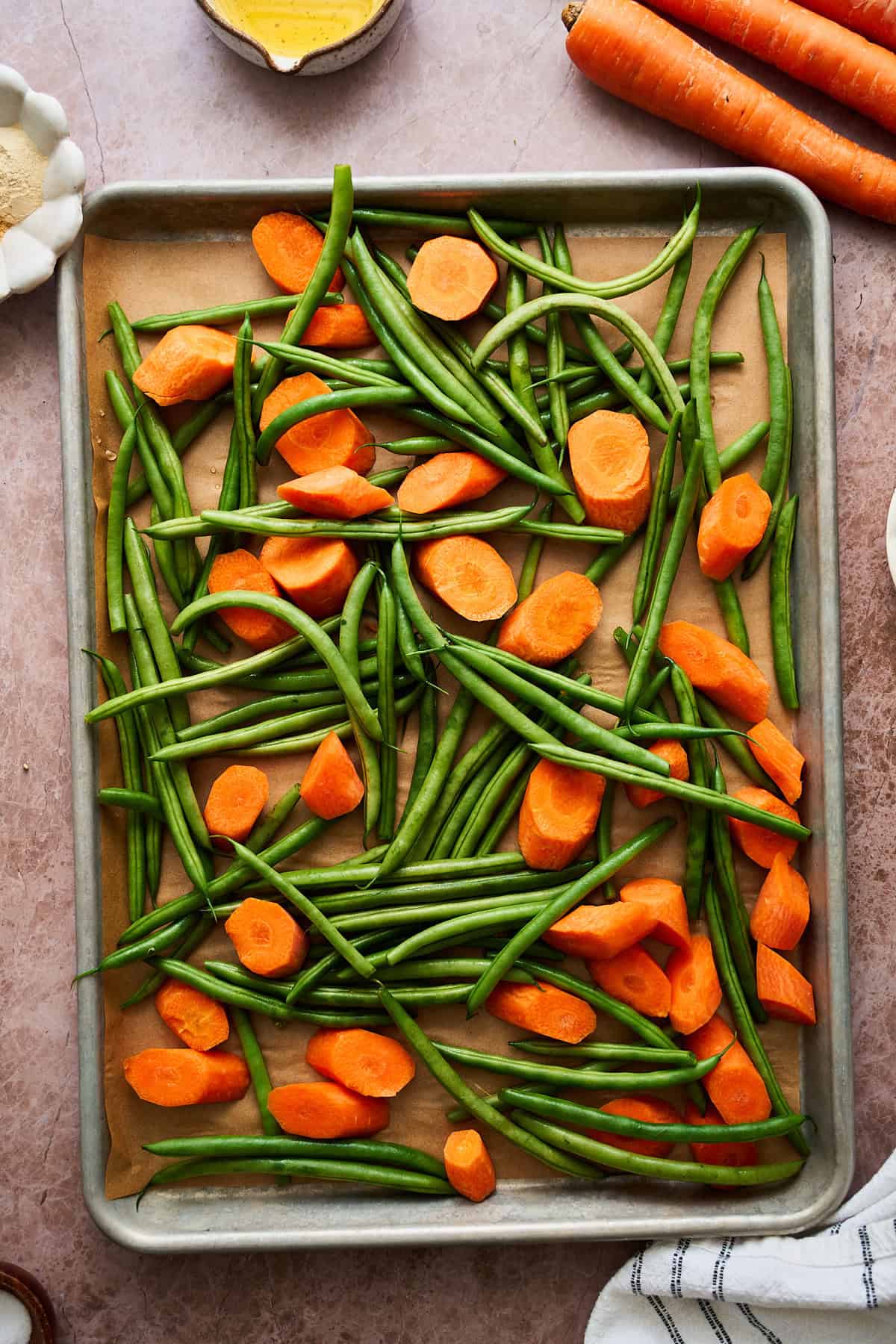 Green beans and carrot rounds on a baking sheet lined with parchment.