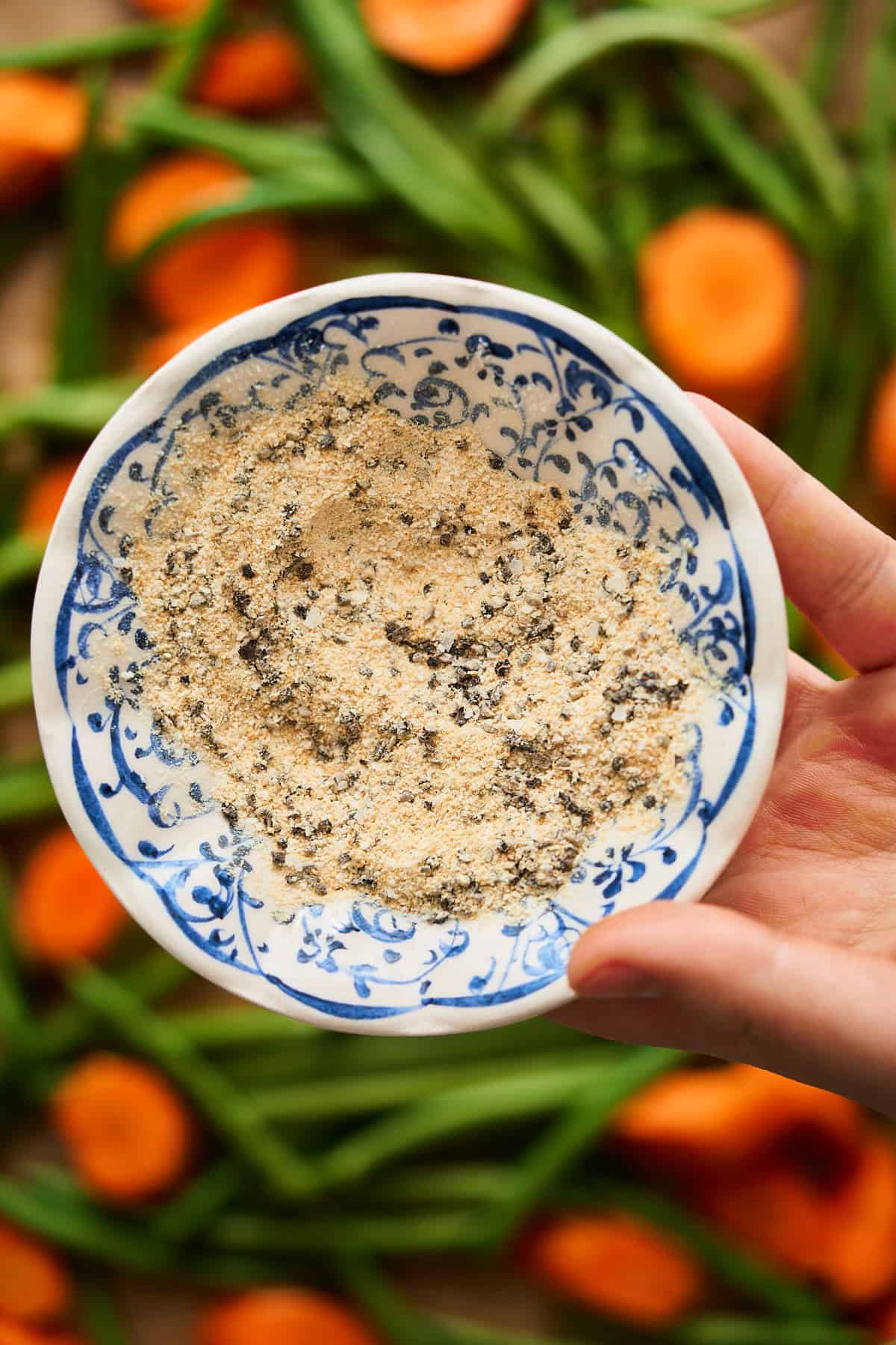 Bowl of seasonings in a small blue and white bowl over carrots and green beans.
