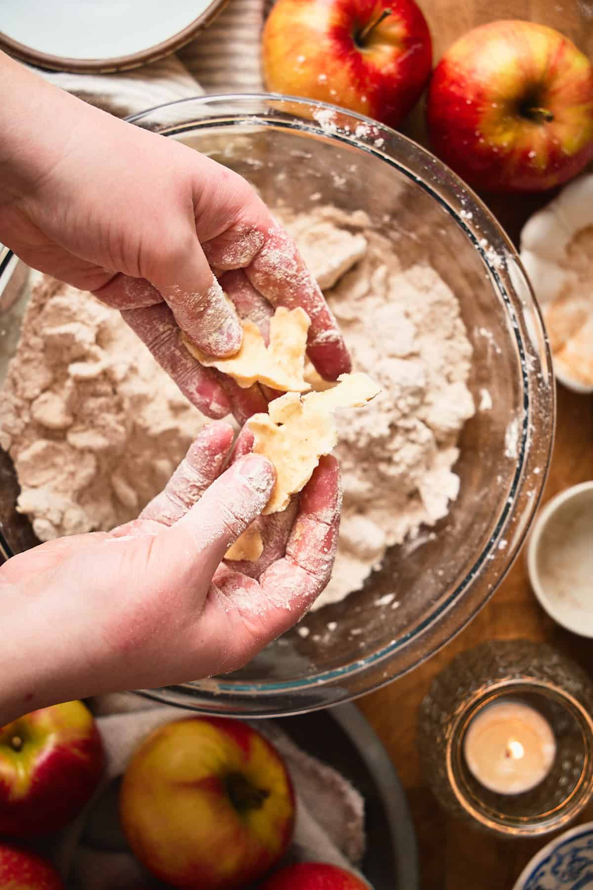 Hand pressing pieces of butter into thin sheets above a bowl with a flour mixture to make biscuits.