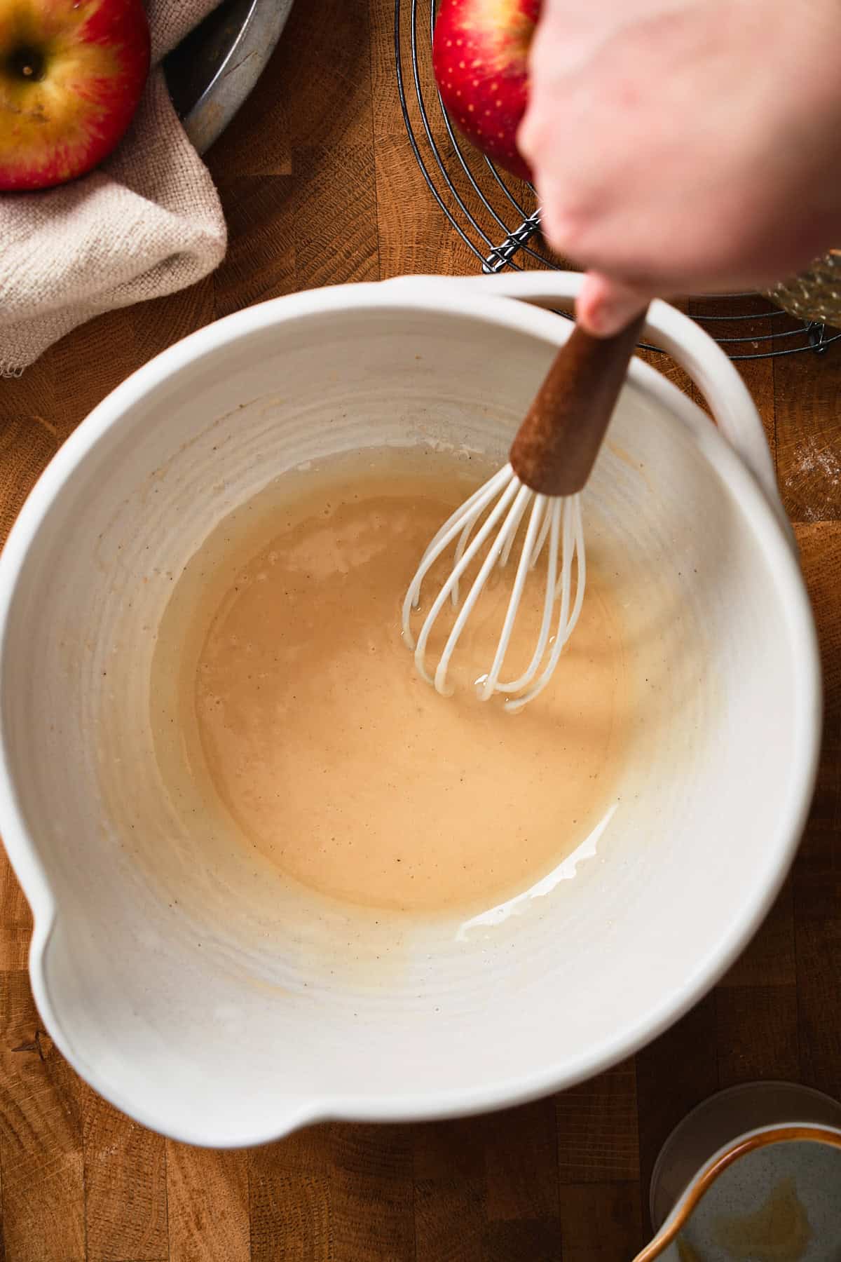 Whisking together apple cider, powdered sugar, salt, and vanilla bean paste in a bowl surrounded by apples and candles.