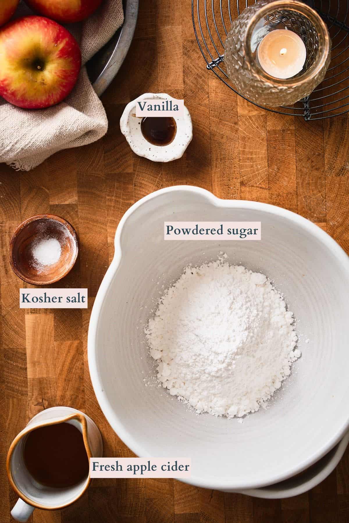 Ingredients to make apple cider glaze laid out on a table surrounded by candles, and apples.
