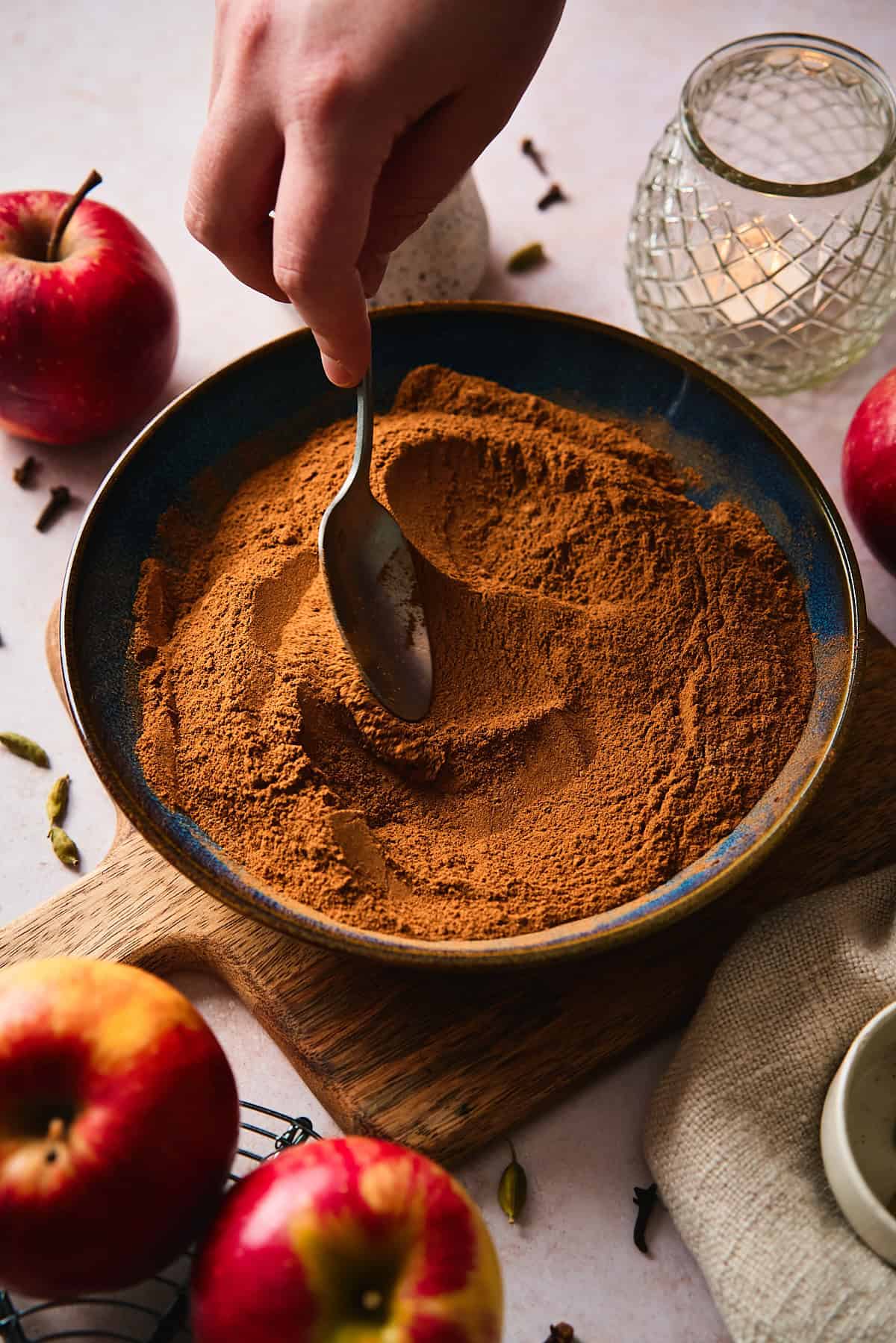 Hand stirring apple pie spice blend with a spoon in a blue bowl.