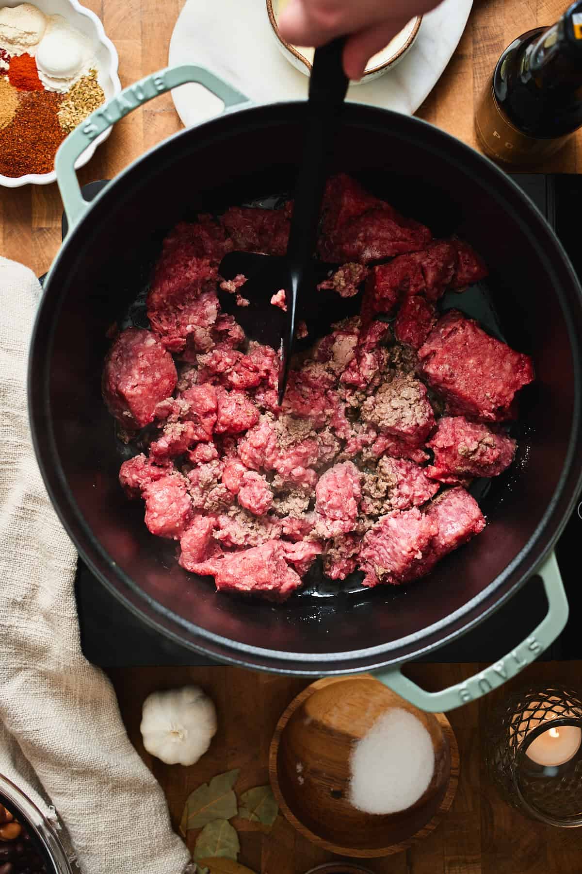 Raw ground beef being broken into crumbles in a Dutch oven.