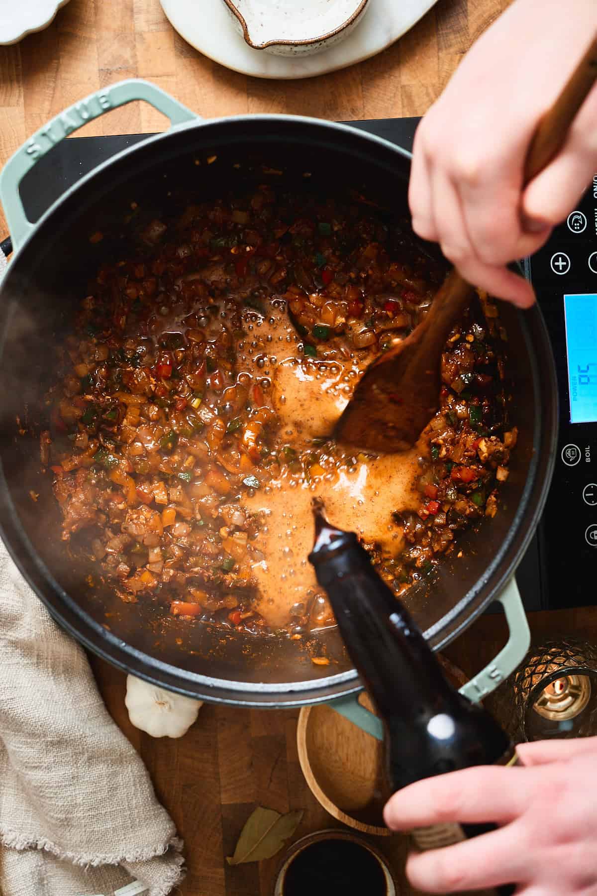 Pouring dark beer into a Dutch oven with sautéed peppers and onions.