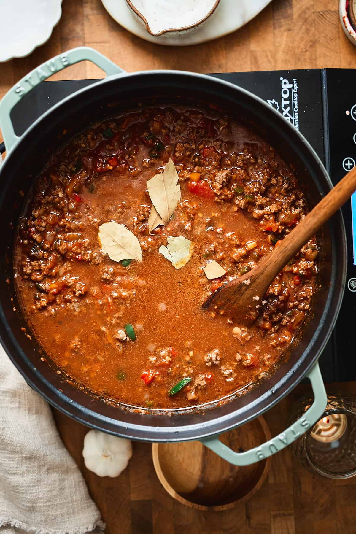 Beer chili simmering in a Dutch oven with bay leaves on top.