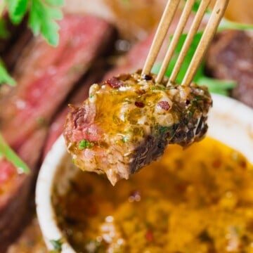Cowboy butter dipping sauce with fresh herbs on a bite of steak.