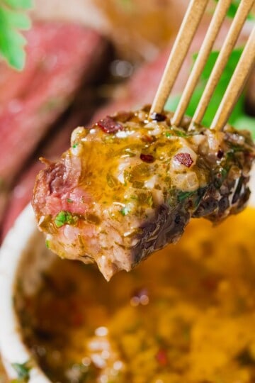 Cowboy butter dipping sauce with fresh herbs on a bite of steak.