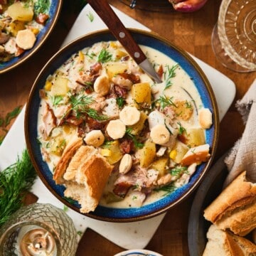 Overhead bowl of creamy whitefish chowder with bacon, potatoes, oyster crackers, dill, and crusty bread.