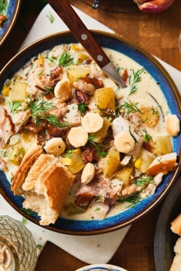 Overhead bowl of creamy whitefish chowder with bacon, potatoes, oyster crackers, dill, and crusty bread.
