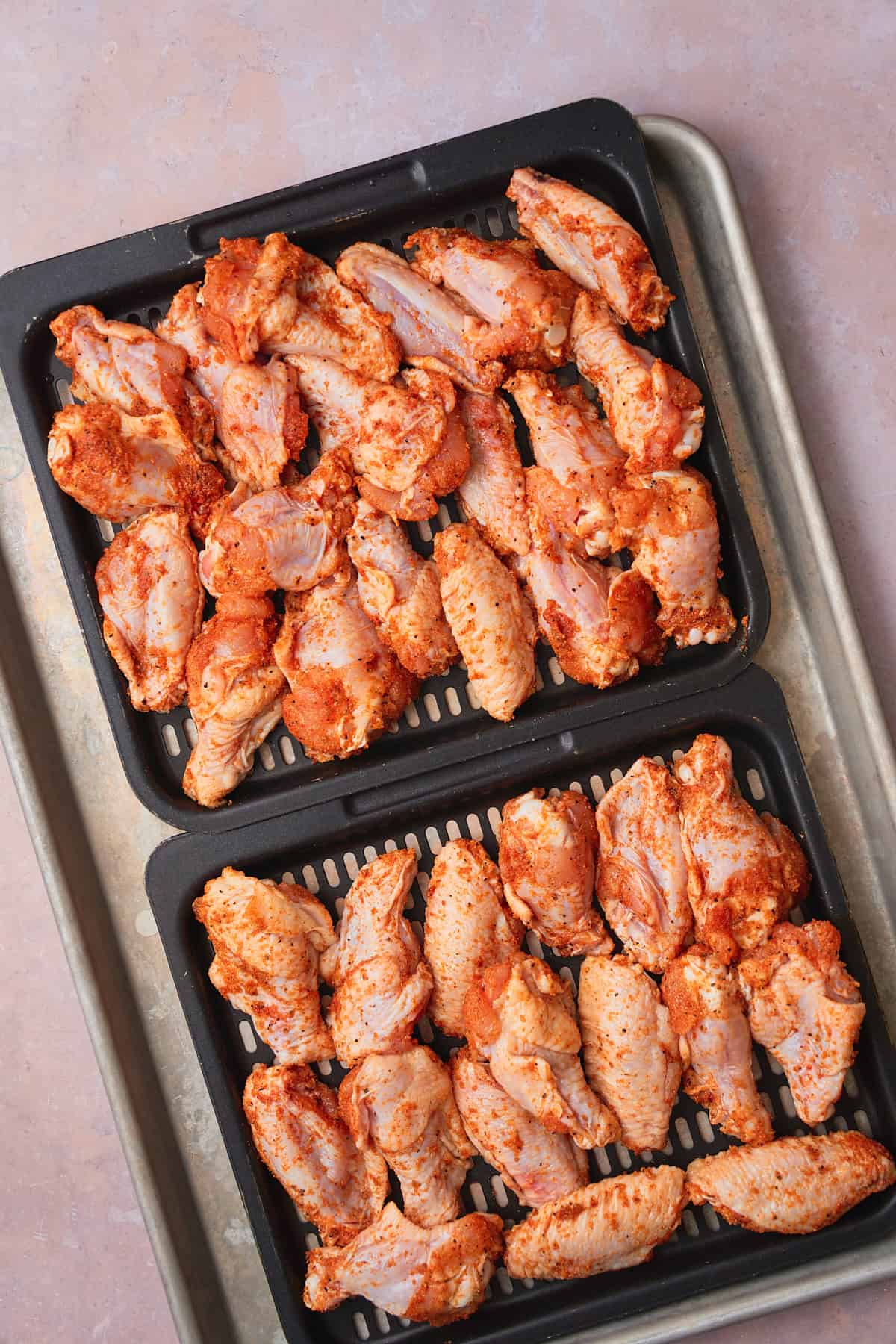 Seasoned chicken wings on air fryer trays.