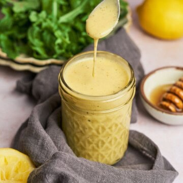 Honey lemon salad dressing in a jar and dressing dripping off a spoon.
