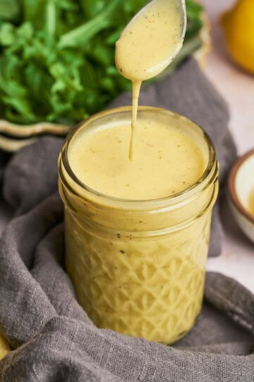 Honey lemon salad dressing in a jar and dressing dripping off a spoon.