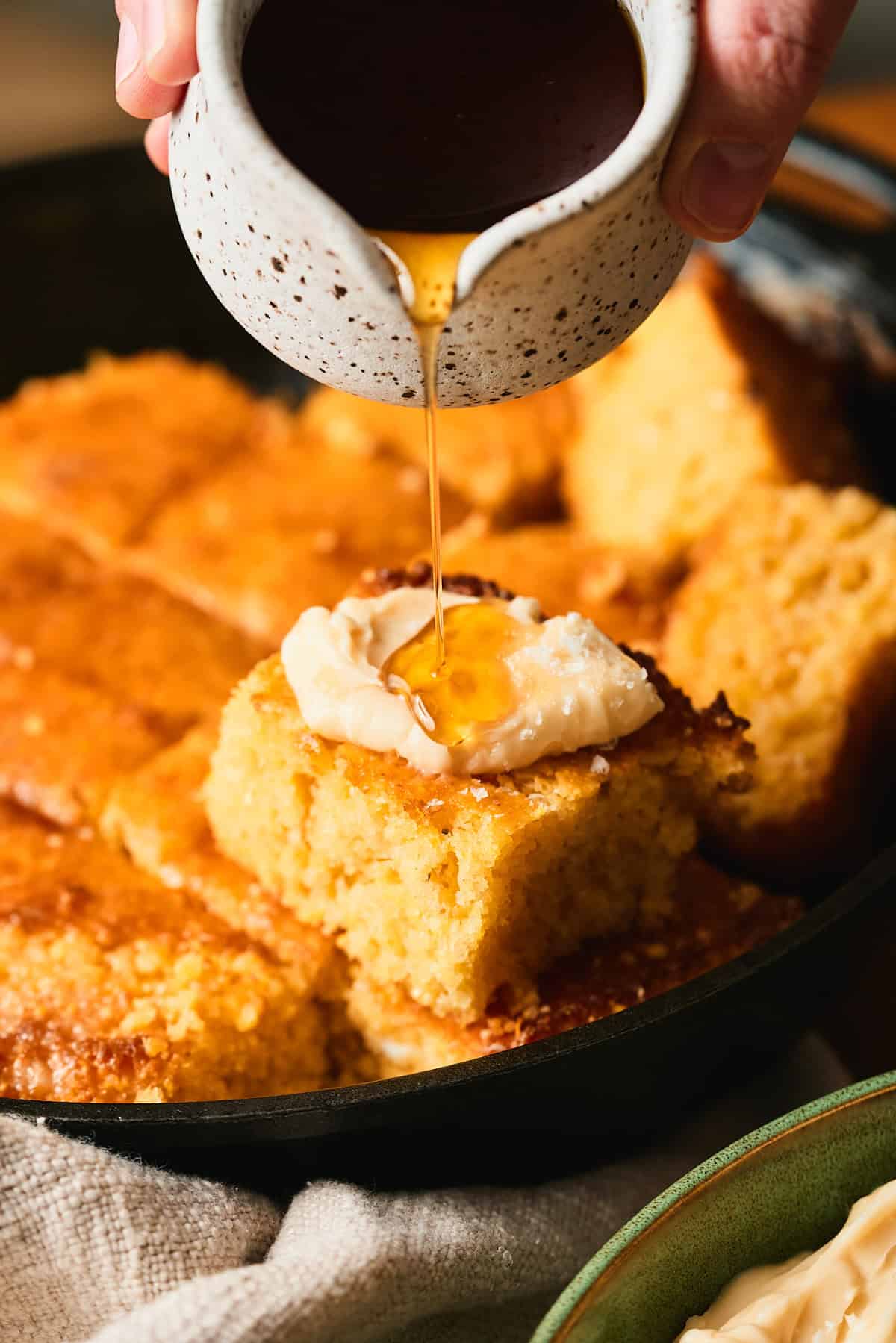 Hand drizzling maple syrup over whipped maple butter on skillet cornbread.