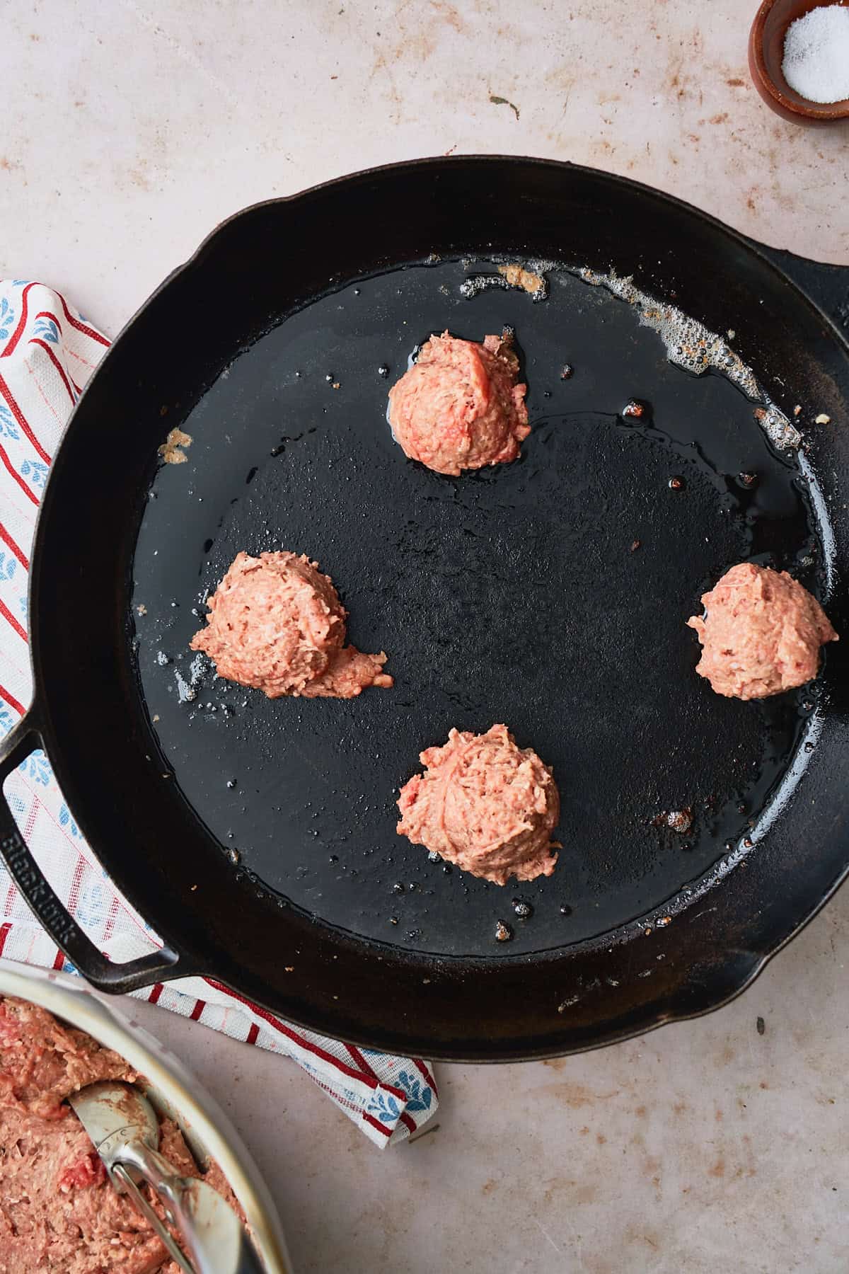 Round meat patties in a hot cast iron skillet with a Nordic napkin underneath.