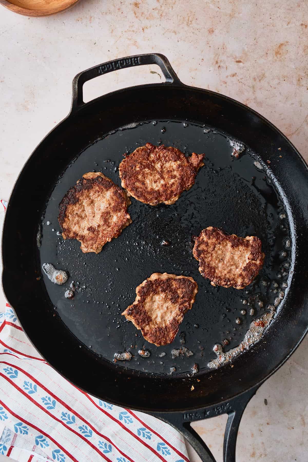 Flat seared meat patties in a hot skillet with a Nordic style linen napkin underneath.
