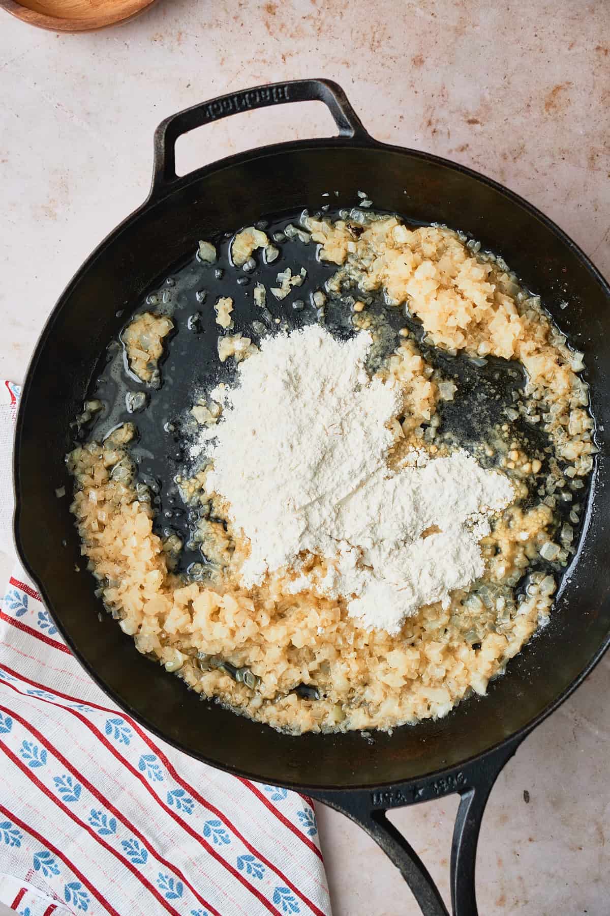 Cast iron skillet with onions cooking in it and flour added to it.